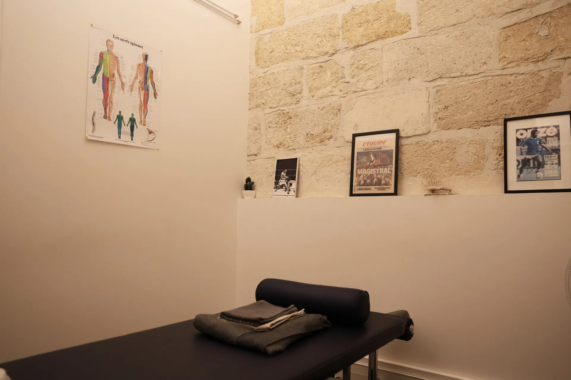 La salle de consultation : table d’ostéopathie, murs de pierre claire, planche anatomique.