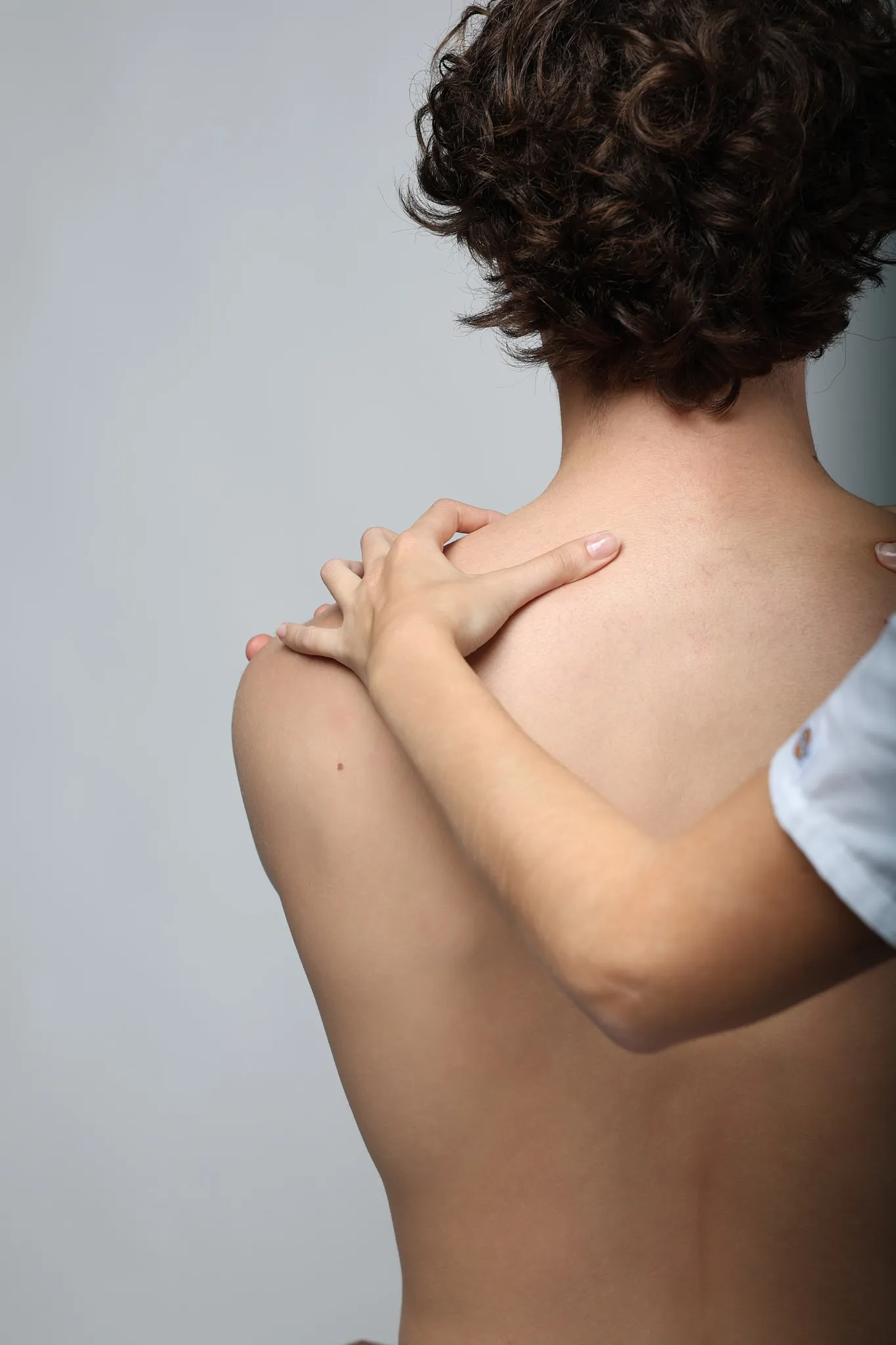 Deux mains posées sur l’épaule et la nuque d’un patient, vu de dos.